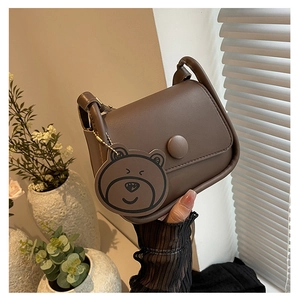 Détail d'un sac besace marron foncé avec boucle ronde et breloque ours adorable