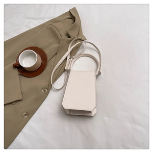 Chic cream trapezoid handbag with round handle and shoulder strap on aesthetic backdrop