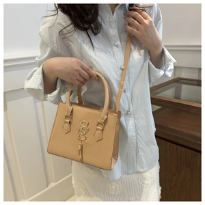 Close-up of light brown crossbody bag with gold double S pendant and tassel detail