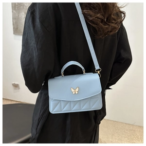 Detail of light blue quilted crossbody bag with silver butterfly clasp and leather texture