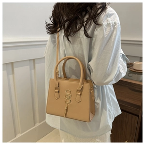 Detail of a chic apricot satchel bag featuring golden metal logo and tassel on the side