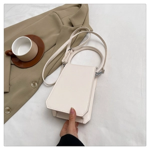 Close-up of a minimalist cream leather handbag on a soft fabric with stitch details