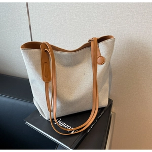 Detail of canvas tote bag showing brown leather handles and circular decorative hardware