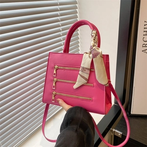 Detail of bright pink PU leather handbag with gold zippers and decorative silk scarf