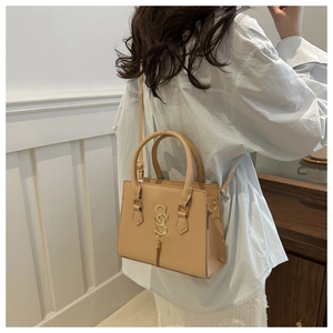 Detail of light beige structured handbag with golden metal logo and fringe on a model