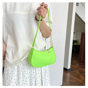 Detail of neon green quilted handbag with gold chain strap on a minimalist model