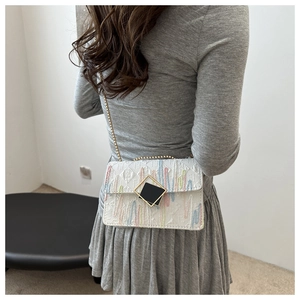Close-up of white crossbody bag featuring colorful stripes and gold square lock