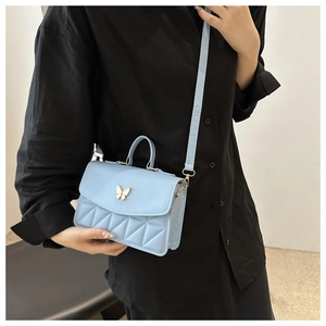 Detail of light blue quilted crossbody bag with gold butterfly buckle on model