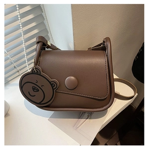 Détail du sac selle en cuir PU marron avec rabat asymétrique et pendentif ours