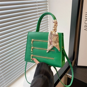 Detailed view of green leather handbag featuring triple zippers and a decorative silk scarf