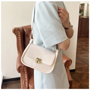 Close-up of a cream quilted crossbody bag with golden clasp shown on a model