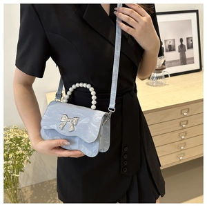 Close-up of light blue pleated bag with pearl handle and silver bow detail on a model