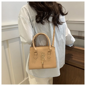 Detail of cream leather handbag with gold S-pendant and fringe against minimalist decor