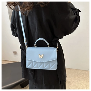 Detail of light blue crossbody bag with quilted texture and gold butterfly clasp