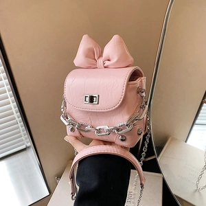 Mini pink crossbody bag with large bow detail and silver chain strap shown in a hand