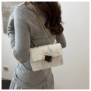 Detail of white crossbody bag with vertical striped embroidery and gold chain strap
