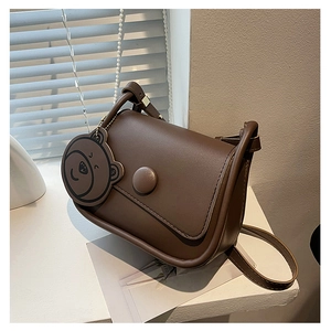 Détail d'un sac besace en cuir marron avec breloque tête d'ours et boucle ronde