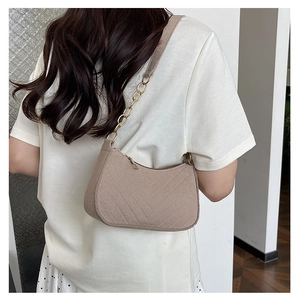 Detail of beige shoulder bag with V-stitch texture and metal chain strap on model