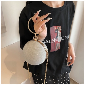 Detail of silver spherical evening bag with gold circular handle and crossbody chain