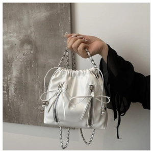 Detail of white leather bucket bag featuring silver zippers, bows and chain strap