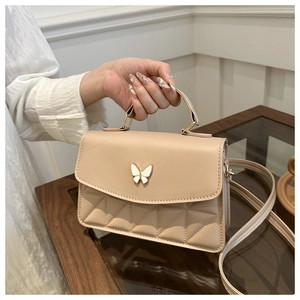 Detail of beige PU leather crossbody bag featuring gold butterfly clasp and quilted pattern