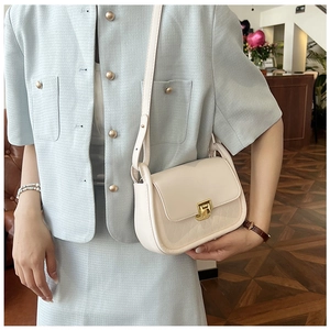 Detail of cream square shoulder bag with quilted pattern and gold twist lock on blue blazer