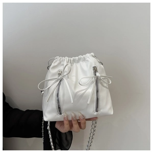 Detail of white leather drawstring bucket backpack with chain strap and bow accents