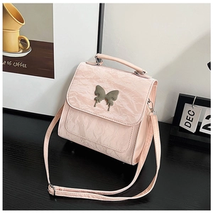 Detail of pink crinkled leather handbag with silver butterfly accent on black table