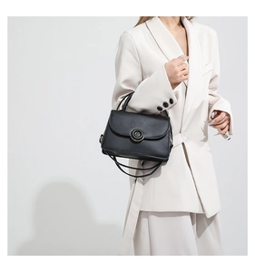 Classic black flap handbag with gold circular hardware shown on a model in a beige suit