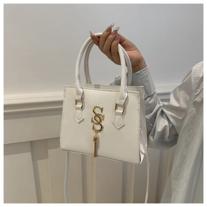 Detail of white PU leather handbag featuring a gold S-shaped logo and metallic tassel