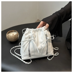 Detail of white drawstring bucket backpack with silver chain straps and bow accents