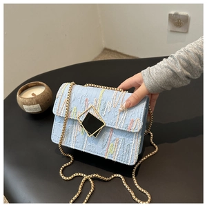 Detail of light blue striped crossbody bag with gold square buckle and chain strap