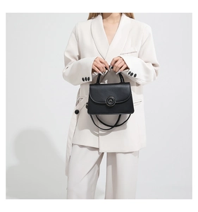 Detail of a minimalist black leather crossbody bag with a round buckle on white business suit
