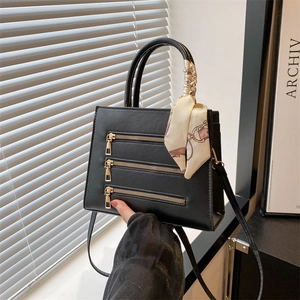 Detailed macro view of black structured crossbody bag with gold zippers and decorative silk scarf