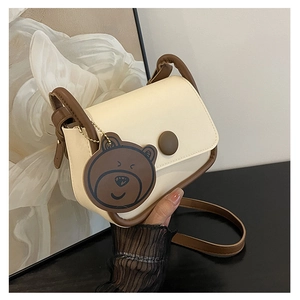 Détail d'un sac besace en similicuir crème avec bordures brunes et breloque ours mignon