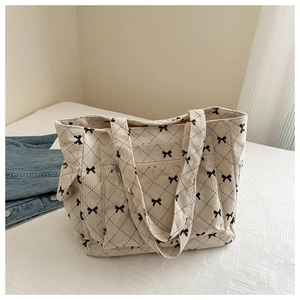 Detail of cream corduroy tote bag featuring quilted diamond pattern and black bow accents