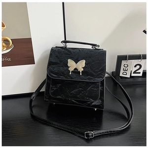 Detail of black textured handbag featuring a gold butterfly metal clasp and top handle