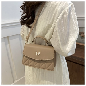 Close-up of beige quilted crossbody bag with decorative butterfly metal buckle on a model