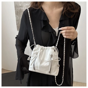 Close-up of a white leather bucket bag with chain strap and bow detail on a black shirt