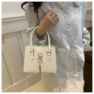 Detail of white square handbag featuring gold SS metal logo and elegant fringe tassel