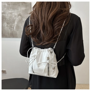 Close-up of white ballet-style bucket bag with silver chain straps and bow detailing