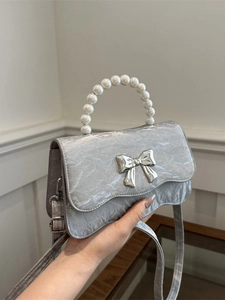 Silver pleated crossbody bag with pearl handle and bow accent shown in hand