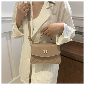 Detail of light brown quilted crossbody bag with white butterfly motif on a female model