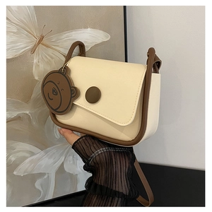 Détail du sac selle crème avec bordure marron, boucle magnétique et breloque petit ours