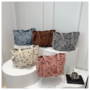 Detailed view of five corduroy tote bags with bow prints on tiered geometric stands