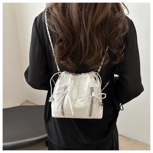 Detail of white drawstring bucket bag with leather bows and silver chain straps