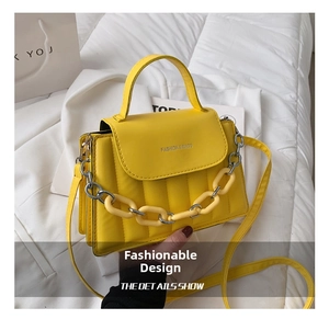 Detail of yellow quilted crossbody bag featuring a thick decorative chain and top handle
