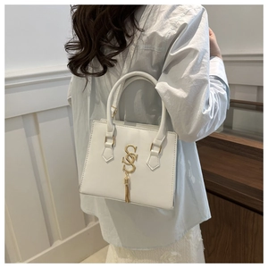 Back view of model wearing white minimalist crossbody bag with gold S-logo and tassel