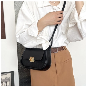 Detail of black saddle bag with textured flap and gold geometric buckle on a model