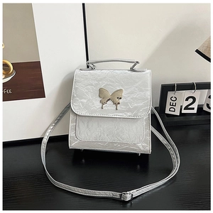 Detail of silver pleated texture bag featuring a fluid gold butterfly metal buckle